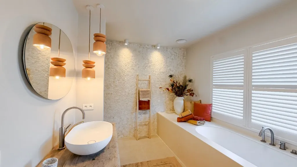 Badkamer met wastafel, steenmuur en ligbad onder shutterramen