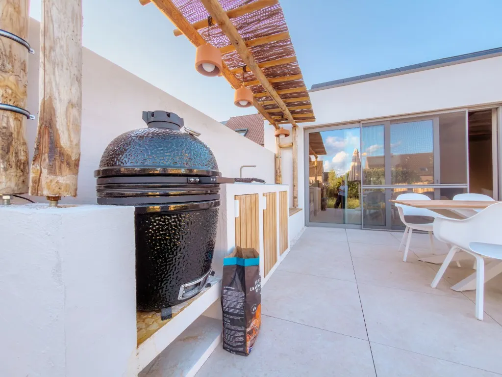 Kamado-barbecue ingebouwd in de witte buitenkeuken onder een houten pergola