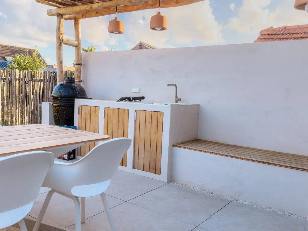 Buitenkeuken met kamado-barbecue, houten kasten en pergola op het terras