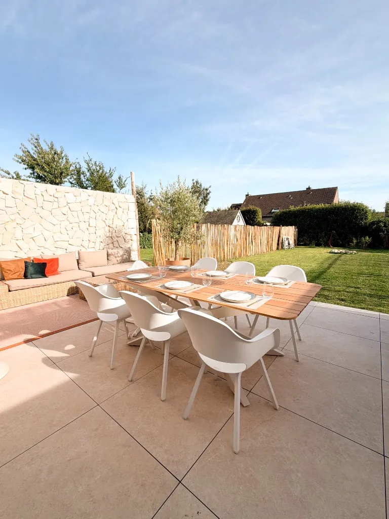 Terras met gedekte eettafel, loungebank tegen steenmuur en omheinde tuin