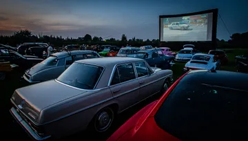 Drive-in openluchtfilm met oldtimers voor een groot scherm in de avond